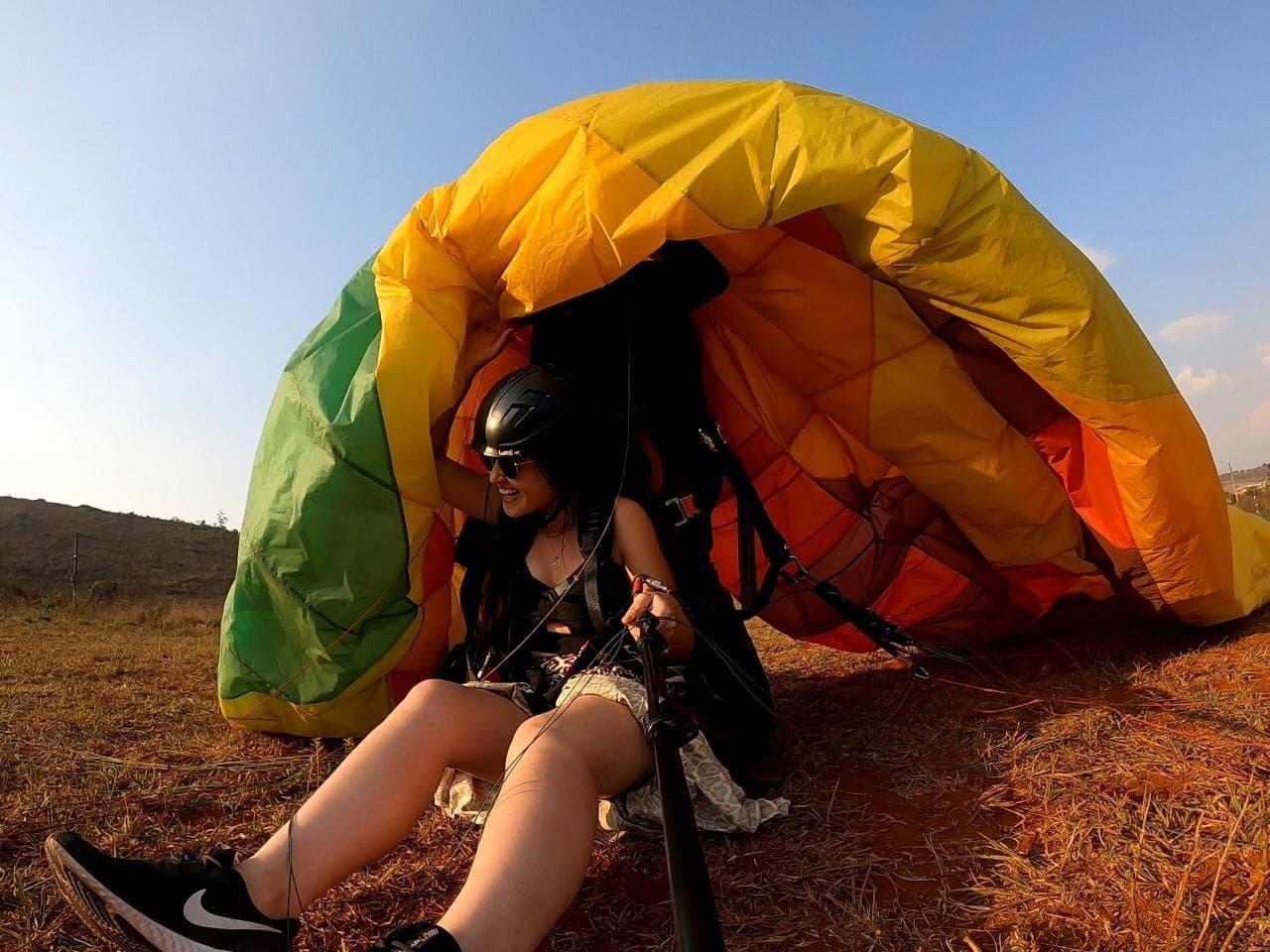 Duas pessoas em voo duplo de parapente sobre a Serra da Moeda, com a paisagem verde ao fundo